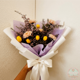 Handheld bouquet of yellow tulips and pale flowers wrapped in lavender and white paper