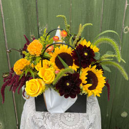 Mixed bouquet with sunflowers, yellow roses, and dark dahlias in a gift bag