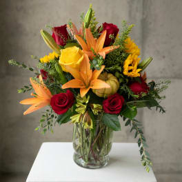 Mixed bouquet of red roses, orange lilies, and yellow flowers in a glass vase