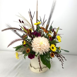 Mixed chrysanthemum arrangement in a cream vase with tall dried grasses
