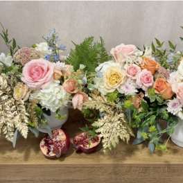 Two pastel floral arrangements in white vases with pomegranates on a table