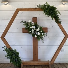 Wooden cross with white flowers and greenery on a hexagonal frame