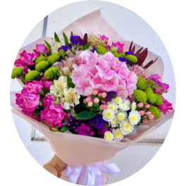 Handheld bouquet of pink, green, white, and purple flowers wrapped in pale paper