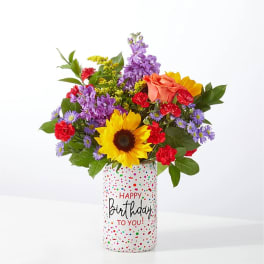 Mixed bouquet in a birthday vase with sunflower, roses, and purple flowers