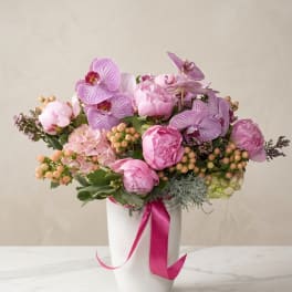 Pink and lavender floral arrangement in a white vase with a ribbon