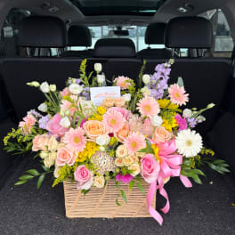 Large mixed flower arrangement in a woven basket with a pink ribbon
