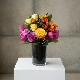 Mixed bouquet of roses, tulips, and daisies in a glass vase