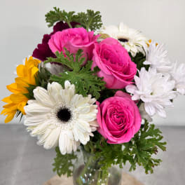 Mixed bouquet of pink roses, white daisies, and yellow flowers in a glass vase