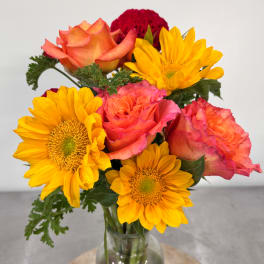 Bouquet of orange roses and yellow sunflowers in a clear glass vase