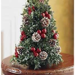 Tabletop evergreen tree decorated with red berries and frosted pine cones on a wooden pedestal table.