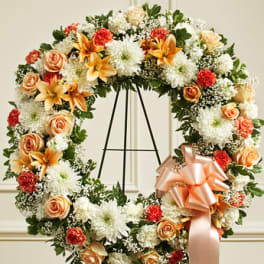 Floral wreath with peach roses, white mums, and orange lilies on an easel