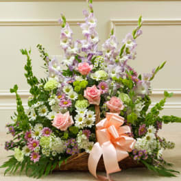 Pastel mixed flower arrangement in a wicker basket with a peach ribbon