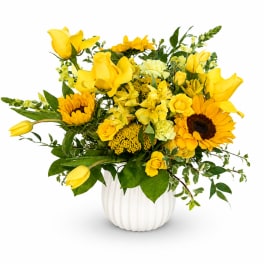 Yellow floral arrangement in a white vase with sunflowers, roses, and tulips
