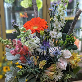Mixed bouquet in a birch bark vase with orange, white, pink, and blue flowers