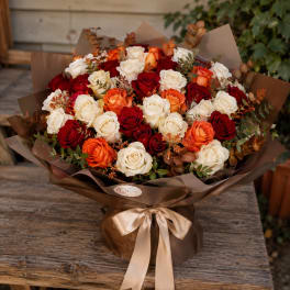 Bouquet of red, white, and orange roses wrapped in brown paper with a satin ribbon