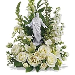 White roses and lilies arranged around a small religious statue