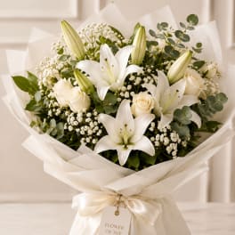 White lilies and roses arranged in a wrapped bouquet with cream ribbon.