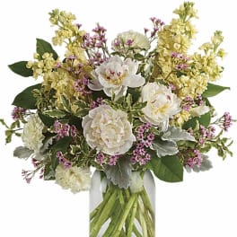 Arrangement of white peonies, yellow stock, and pink filler flowers in a clear glass jar vase