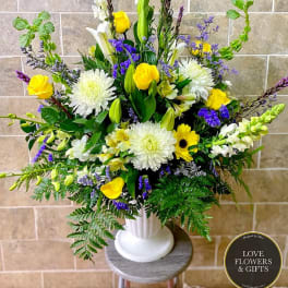 Tall yellow, white, and purple flower arrangement in a white pedestal vase