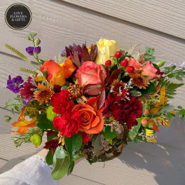 Low arrangement of red and orange roses and carnations with yellow accents in a rustic basket
