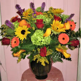 Mixed bouquet of roses, sunflowers, calla lilies, and gerbera daisies in a dark vase