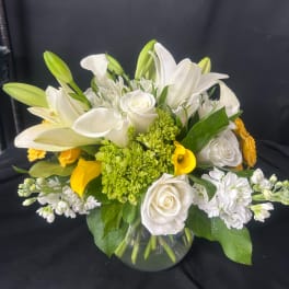 White lilies, roses, and yellow calla lilies in a glass vase