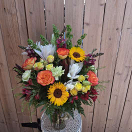 Mixed bouquet with sunflowers, roses, and white lilies in a glass vase