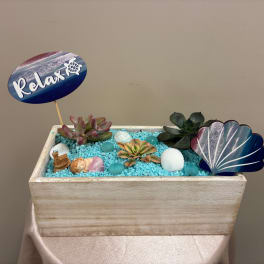 Succulent arrangement in a wooden box with a "Relax" sign and seashell accents