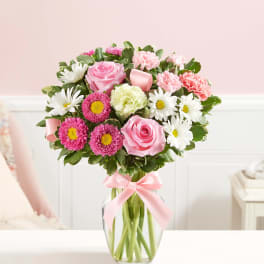 Pink and white mixed bouquet in a clear glass vase with a pink ribbon