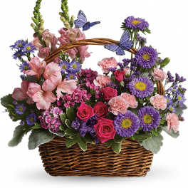 Wicker basket of pink and purple mixed flowers with two decorative blue butterflies