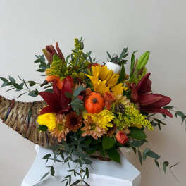 Cornucopia basket arrangement with red lilies, yellow blooms, and pumpkins