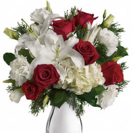 Arrangement of red roses, white lilies, and white flowers in a shiny silver vase