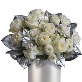 Compact white arrangement of roses, carnations, and mums in a white cylinder vase with silver leaves.