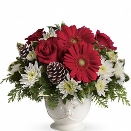 Red gerbera daisies, red roses, and white mums with pinecones in a white ceramic footed bowl