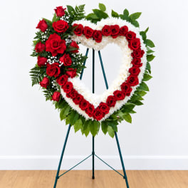 Heart-shaped standing floral wreath with red roses and white flowers on an easel