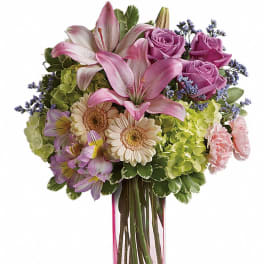 Tall pink and lavender mixed bouquet with lilies, roses and daisies in a clear pink glass vase