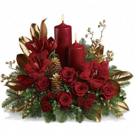 Holiday centerpiece with red roses, red amaryllis, and two red pillar candles accented with gold cones and berries.