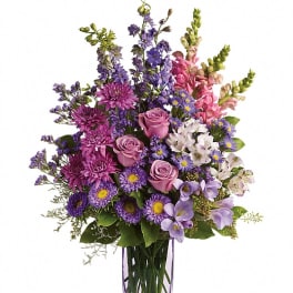 Tall bouquet of pink roses and purple mixed flowers in a slender lavender glass vase