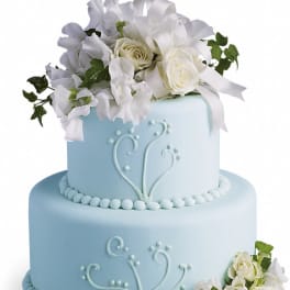 Two-tier light blue cake decorated with white roses and white flowers on top and at the base.