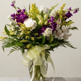 Mixed bouquet of purple, white, and yellow flowers in a glass vase