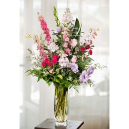 Tall mixed bouquet of pink, lavender, and white flowers in a clear glass vase