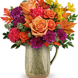 Mixed bouquet of orange, pink, and purple flowers in a metal pitcher