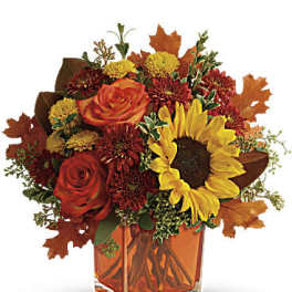 Autumn bouquet of red roses and a sunflower in a square glass vase