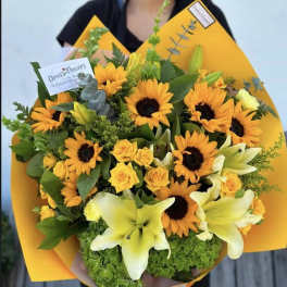 Bouquet of yellow sunflowers, roses, and lilies wrapped in bright orange paper