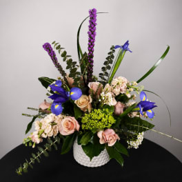 Mixed bouquet with pink roses, blue irises, and purple spikes in a white vase