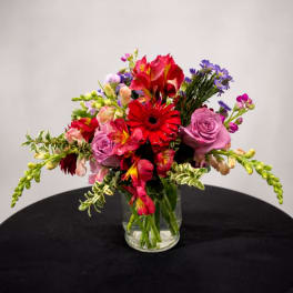 Mixed bouquet of red, pink, and purple flowers in a clear glass vase