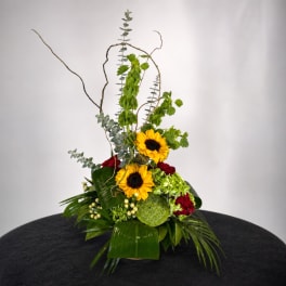 Tall floral arrangement with sunflowers and red roses in a low container