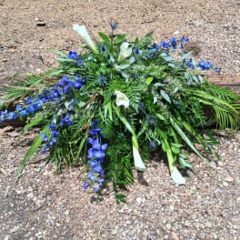 Blue and white floral spray with calla lilies and greenery on the ground