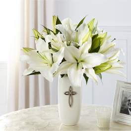White lilies arranged in a tall white vase with a cross emblem