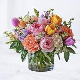 Mixed bouquet of pink, orange, yellow, and purple flowers in a clear glass vase